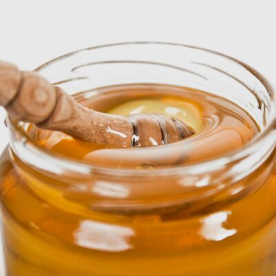 A detailed close-up of a wooden honey dipper in a jar filled with golden honey.