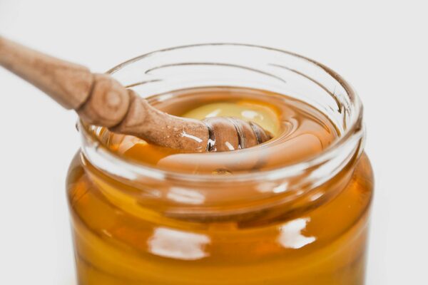 A detailed close-up of a wooden honey dipper in a jar filled with golden honey.