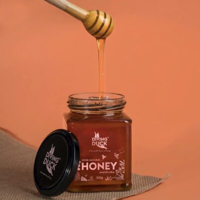 Close-up of a honey dipper and jar on an orange background, perfect for culinary uses.