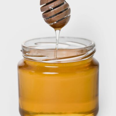 Rich golden honey dripping from a wooden dipper into a glass jar, highlighting its sweet and sticky texture.
